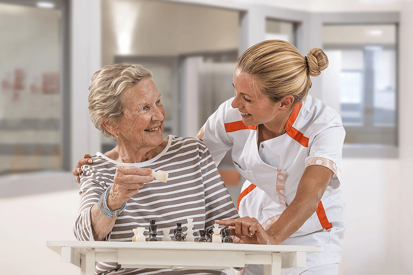 Young homecarer playing chess with elderly woman